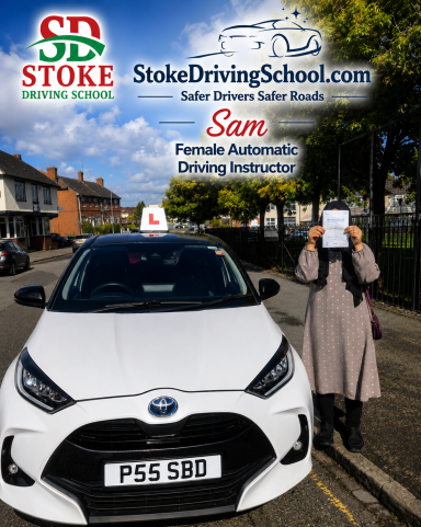 A person holds a driving certificate next to a white car with a learner plate.