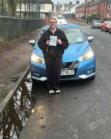 Person holding a document in front of a blue car parked on a residential road.