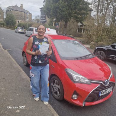 A person holding documents stands next to a red taxi on a street.