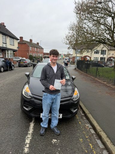 A man holding a document stands next to a parked black car on a street.