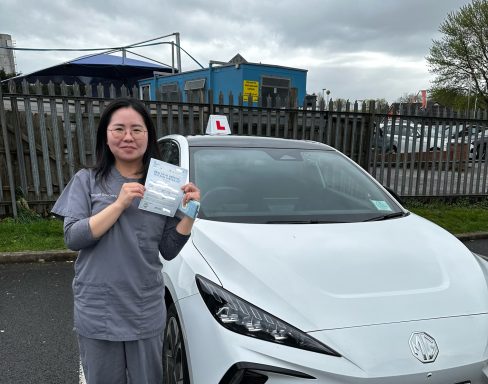 A person smiling and holding a document next to a white car with a learner driver sign.