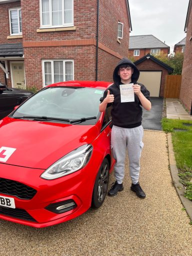 Person holding driving test pass certificate beside a red car with an "L" plate.