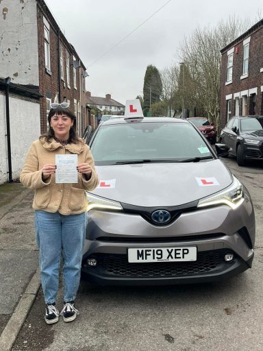 A person holding a certificate stands in front of a car with learner driver signage.