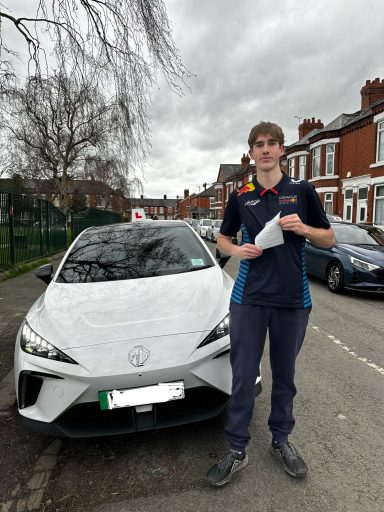A young man in a blue shirt stands beside a white car on a residential street.