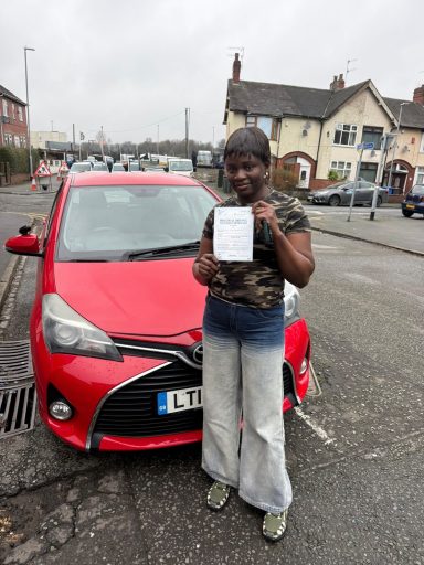 A person holds a document next to a red car on a street.