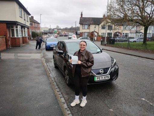 A person stands beside a black car, holding a document on a residential street.