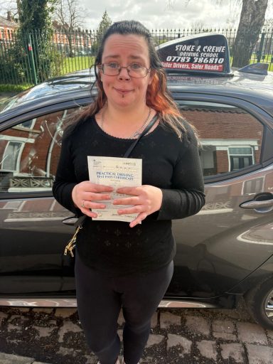 A woman holding a book stands in front of a parked car.