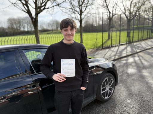 Young man holding a certificate beside a black car in a sunny outdoor setting.