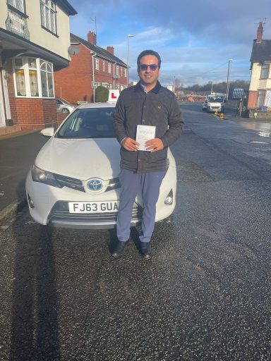 A man stands outside holding a document in front of a white car on a street.