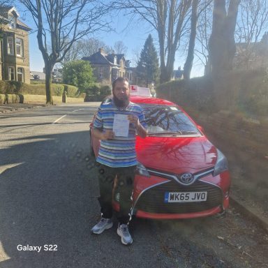 Man holding a document stands beside a red car on a sunny street.
