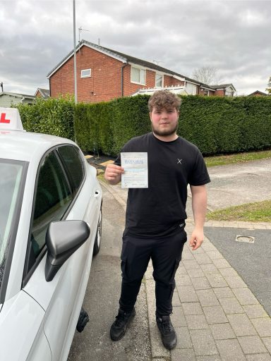 A young man in a black shirt holds a certificate next to a driving school car.