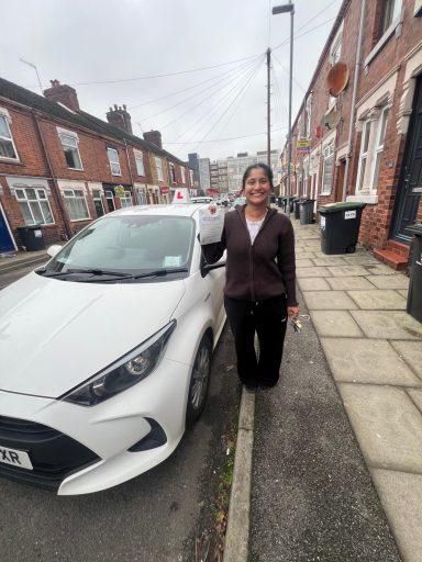 A woman stands beside a white car on a residential street.
