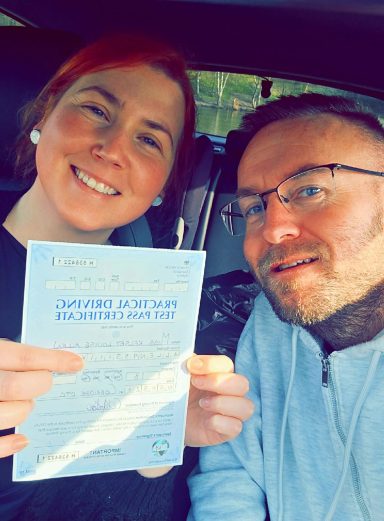 A couple smiling, holding a certificate inside a car.