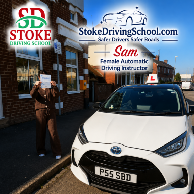 A female driving instructor holds a sign beside a car with a learner plate outside a driving school.