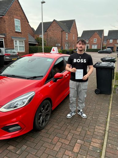A person holding a certificate stands beside a red car on a residential street.