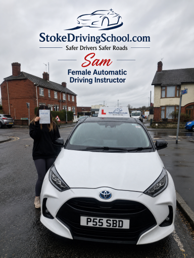 A person holds a sign in front of a white car marked for a driving school in a residential area.