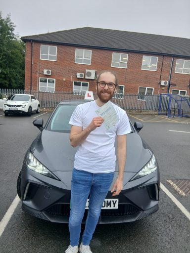 Man in a white shirt holding a document, standing in front of a black car.