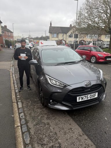 A man stands next to a grey car parked on a street.