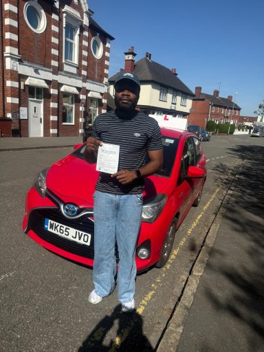 Person holding a driving test certificate next to a red car on a street.