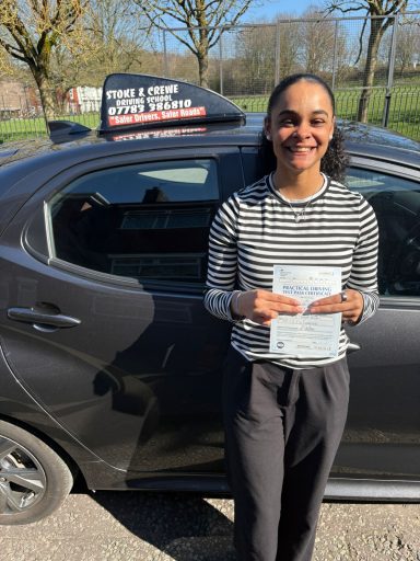Smiling woman holding leaflets next to a car in a sunny outdoor setting.