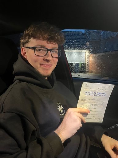 Young man in a hoodie smiles while holding a document inside a car.