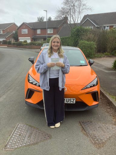 A woman stands in front of an orange car on a residential street.