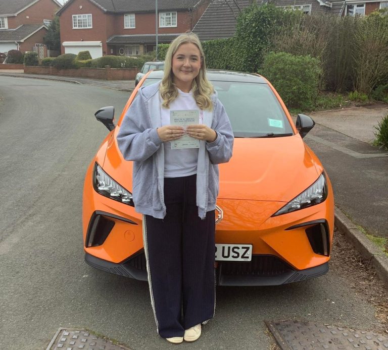 Young man holding a document in front of an orange car, parked on a residential street.