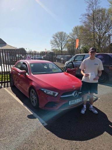 A person stands next to a red car parked in a sunny area.