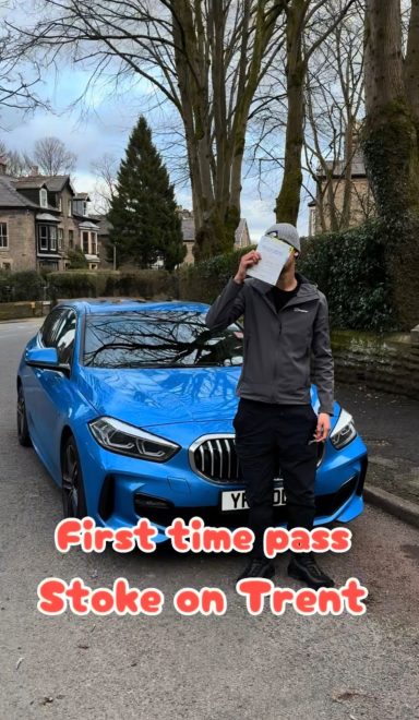 A person holding a certificate stands beside a blue car on a street.