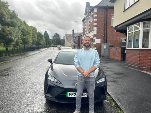 A man stands in front of a black car on a rainy street.