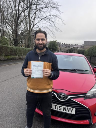 Man holding a certificate stands beside a red Toyota car in a suburban area.