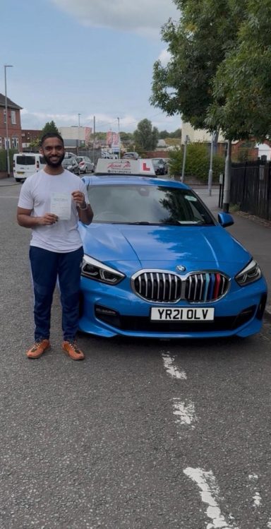 A man stands next to a blue car on a residential street.