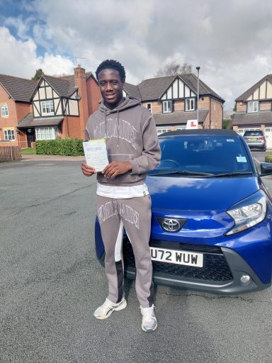 A person in sportswear holds a document next to a blue car in a residential area.