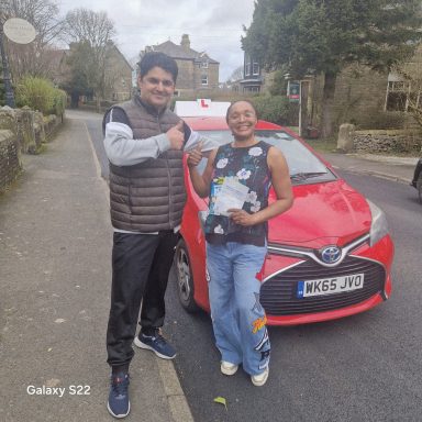 Two people stand beside a red car on a street, smiling and holding a trophy.