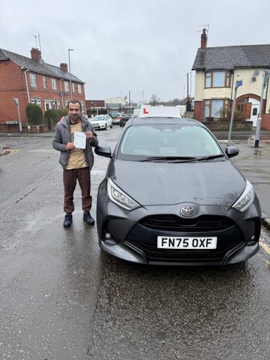 A person holding a certificate stands next to a grey Toyota car in a residential area.