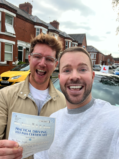 Two smiling men holding a certificate outside a house on a cloudy day.