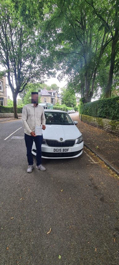 A person stands beside a white car on a tree-lined street.