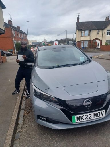 Person standing by a grey Nissan car on a residential street.