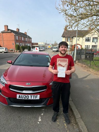 Man holding a certificate stands next to a red car on a street.