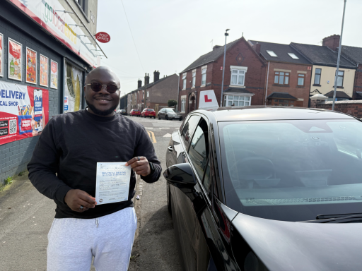 Smiling man holding a certificate next to a parked car on a residential street.