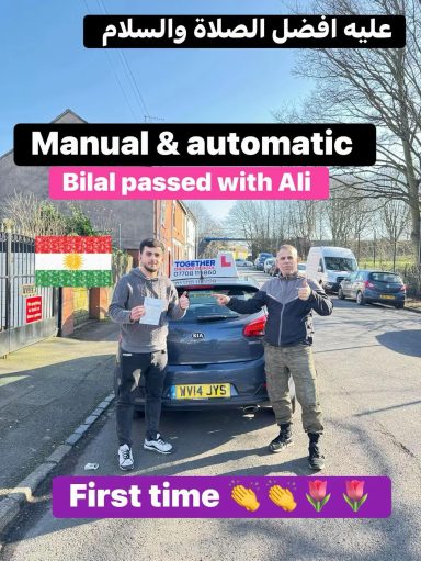 Two men celebrate a driving test pass, standing by a car with a flag in the background.