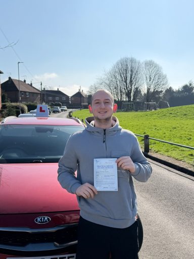 Person holding a certificate in front of a red car on a sunny day.
