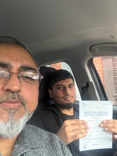 Two men in a car, one holding a document and looking at the camera.