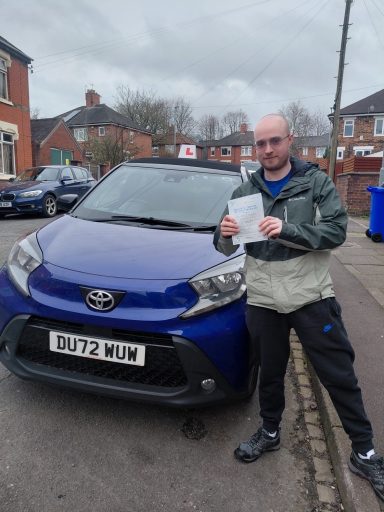 Person holding a document outside a blue Toyota car on a residential street.