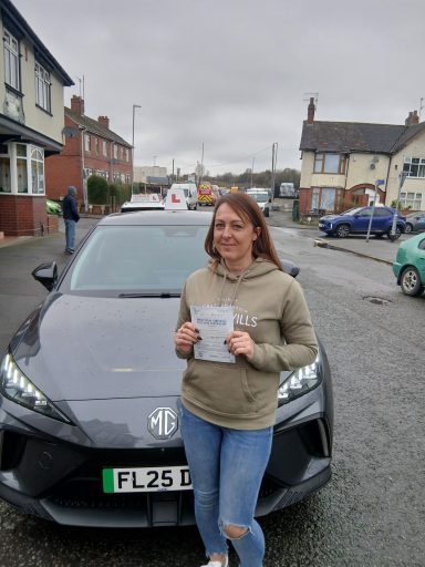 A woman smiles next to a black car, holding a document, on a residential street.