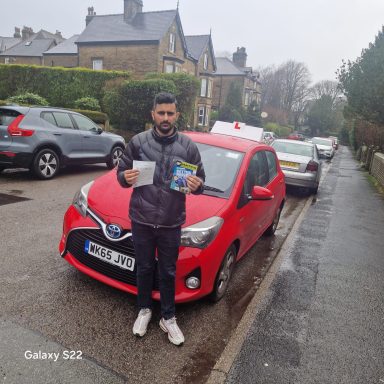A man holding documents stands by a red car on a residential street.