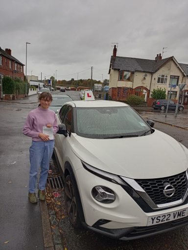 A person holding a paper stands beside a white car with a learner driver sign.
