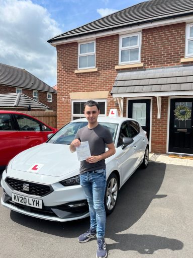 A person stands holding a certificate next to a white car outside a house.